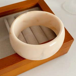 Detailed shot of beige marble resin bangle with wide thick walls in a wooden box
