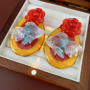 Macro detail of goldfish and red rose resin earrings inside a wooden jewelry box