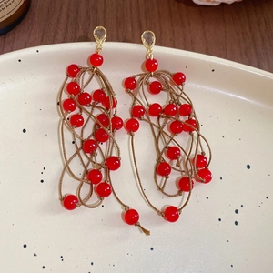 Close-up of red beaded long tassel earrings with brown braided rope on a ceramic tray