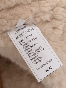 Care label on faux shearling jacket showing 100% polyester and washing instructions