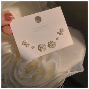 Close-up of pearl camellia and bow earring set on display card with gold accents