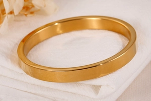 Detailed shot of polished gold stainless steel bangle on white fabric with dried flowers