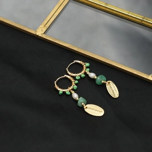 Long pearl earrings with green beads and handmade tag on black textured fabric