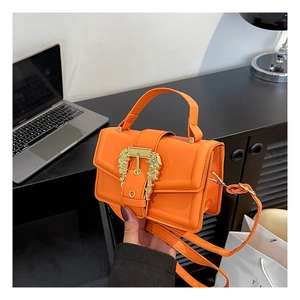 Detail of bright orange leather handbag featuring a golden lion head buckle and handle