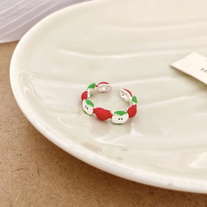Macro shot of silver ring with red and green enamel apple design on white ceramic base