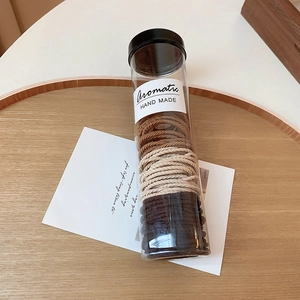 Set of multi-colored elastic hair ties in a clear cylinder box on a wooden tray