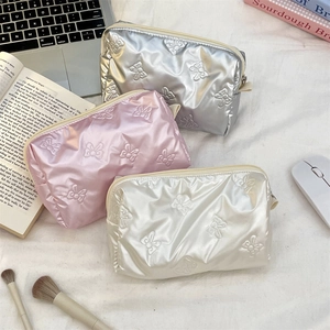 Detailed trio of quilted bow pattern cosmetic bags in silver, pink, and cream colors