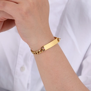 Close-up of a gold Cuban link chain bracelet with a blank rectangular plaque on a wrist