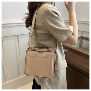 Close-up of the beige tote bag featuring RICH RABBIT embossed text and a wide shoulder strap