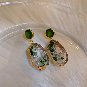 Close-up of irregular gold earrings with green emerald stones on a glass plate