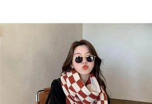 Close-up of a model wearing a red and white checkerboard knit scarf with gold sunglasses