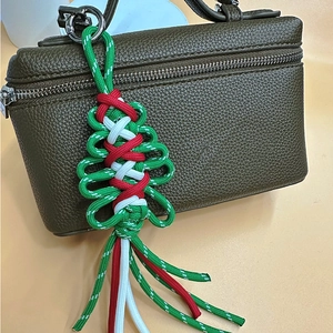 Handmade woven Christmas tree charm with tassels and metal clip on a green leather bag