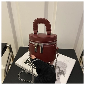 Gros plan du sac à bandoulière cylindrique bordeaux avec chaîne argentée et cuir mat