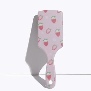 Detail of pink massage hairbrush with cute strawberry prints and ergonomic handle