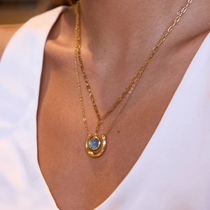 Close-up of double layer gold necklace with horseshoe pendant and blue gemstone inlay