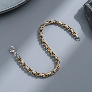 Macro view of two-tone Byzantine chain bracelet with silver lobster clasp on grey surface