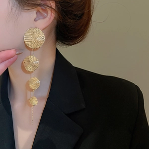 Detailed view of long gold tassel earrings with textured circular metal discs on model