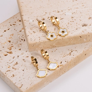 Elegant gold flower drop earrings with white petals on natural beige stone background