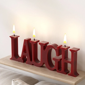 Detailed view of red LAUGH letter-shaped candle burning on a rustic wooden stand