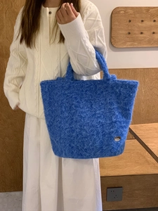 Dettaglio di borsa tote in peluche blu con ciondolo a cuore argento e trama morbida