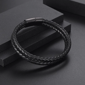 Double-layered black braided leather bracelet with black magnetic clasp on dark pedestal