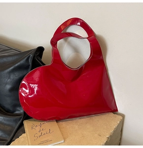 Macro shot of red heart-shaped patent leather handbag on a stone base with glossy finish