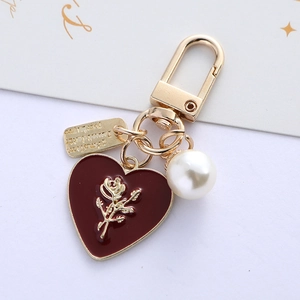 Detail of heart charm with rose relief, pearl pendant and metal tag on gold keychain