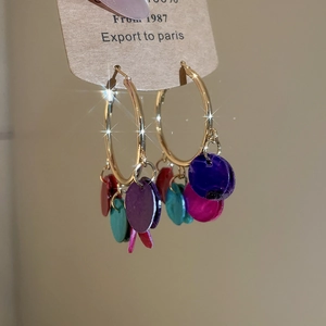 Detail showing colorful stone pendants and gold hoop earrings with sparkling texture