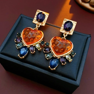 Close-up of vintage gold earrings with heart-shaped orange gems and colorful crystals