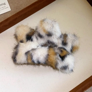 Detail showing plush leopard print hair claw clip on soft beige fabric background