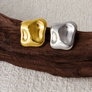 Macro shot of irregular lava-shaped gold and silver stainless steel stud earrings on wood