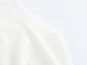 Detailaufnahme von weißem Netzstoff mit eleganten Perlenverzierungen auf dem Kleid