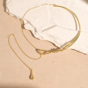 Detail of a minimalist gold twisted necklace with a glossy teardrop pendant on stone