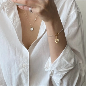 Close-up of a layered S925 silver heart bracelet and pearl necklace on a model