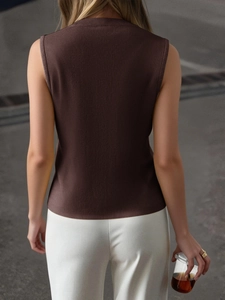 Rear view of a woman wearing a brown sleeveless Y2K knit vest top against a street backdrop