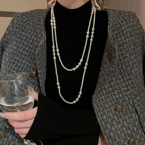 Close-up of layered white pearl necklace worn on a black turtleneck and tweed jacket