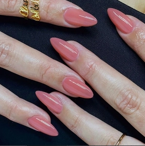 Close-up of almond-shaped mauve pink press-on nails with high-gloss finish and gold ring