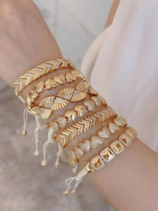 Gestapelde gouden boho-armbanden met hartjes en waaiers aan verstelbare koorden.