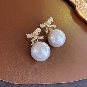 Macro shot of bowknot earrings with white pearls and sparkling zircons on leather