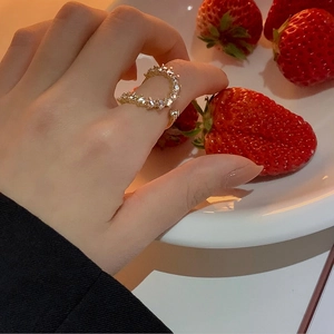 Close-up of gold heart-shaped ring with clear cubic zirconia on hand near strawberry bowl