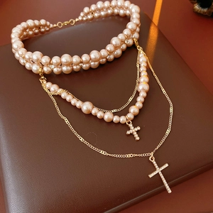 Macro detail of multi-layer gold pearl necklace with rhinestone cross pendants on leather