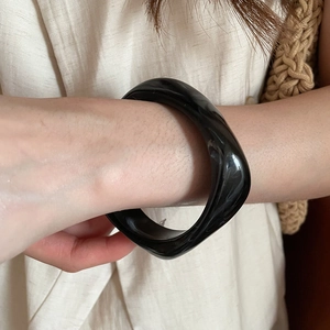Close-up of a glossy black irregular resin bangle worn on wrist over linen fabric