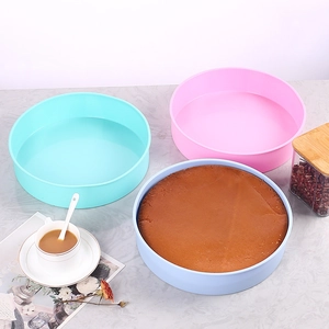 Three round silicone cake molds in pink and blue on a stylish marble kitchen countertop