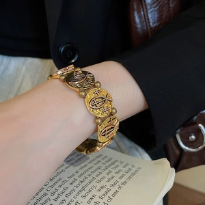Macro detail of vintage gold coin bracelet featuring embossed fish and cross religious icons