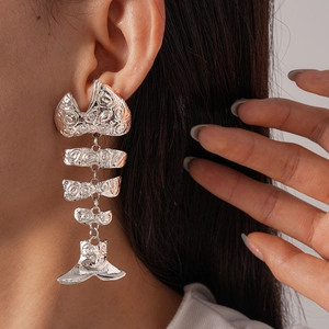 Close-up of oversized silver metal fishbone earrings with textured hammered finish