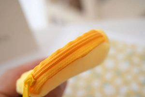 Macro view of the yellow plush coin purse featuring a color-matched smooth metal zipper