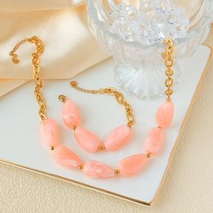 Detailed view of chunky gold chain jewelry set with pink marble stones on a white tray