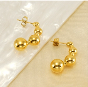 Dettaglio di orecchini a pisello in oro 18K con sfere graduate su tessuto strutturato