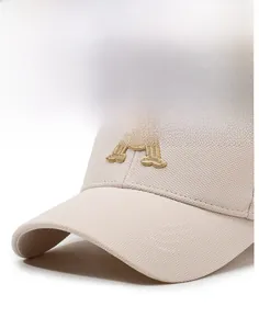 Detailed close-up of cream baseball cap with gold embroidered letter A and twill fabric