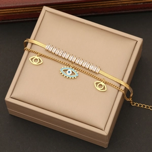 Golden double-layer bracelet with zircon stones and blue evil eye enamel charms on a jewelry box